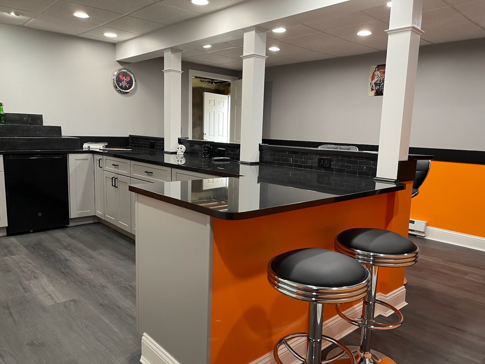Modern kitchen area in a newly built in-law suite addition in Tolland, Connecticut, featuring black countertops, white cabinets, and orange accent walls.